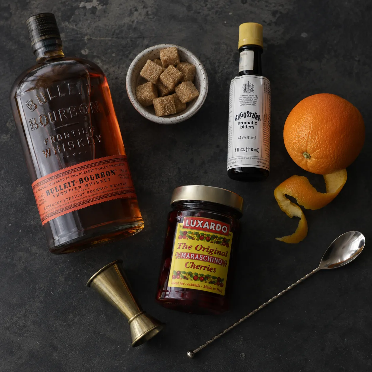Old fashioned ingredients flatlay with bourbon, bitters, sugar cubes, and orange