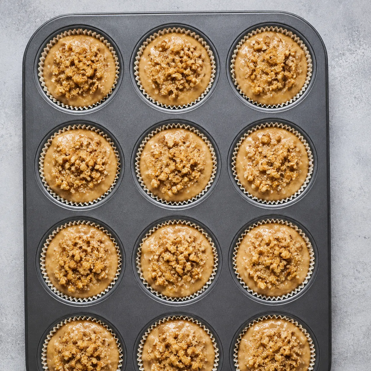 Banana nut muffin batter in a muffin tin topped with chopped walnuts