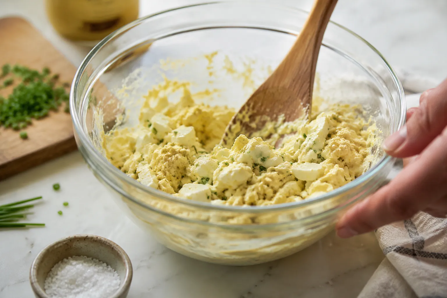 Mixing creamy egg salad in glass bowl with mayo and Dijon