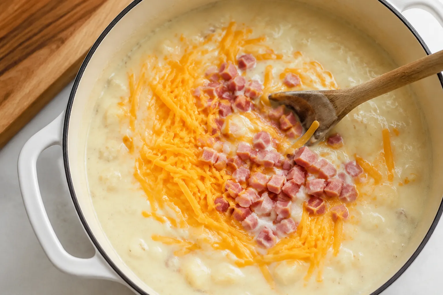 Stirring cheddar and diced ham into creamy potato soup