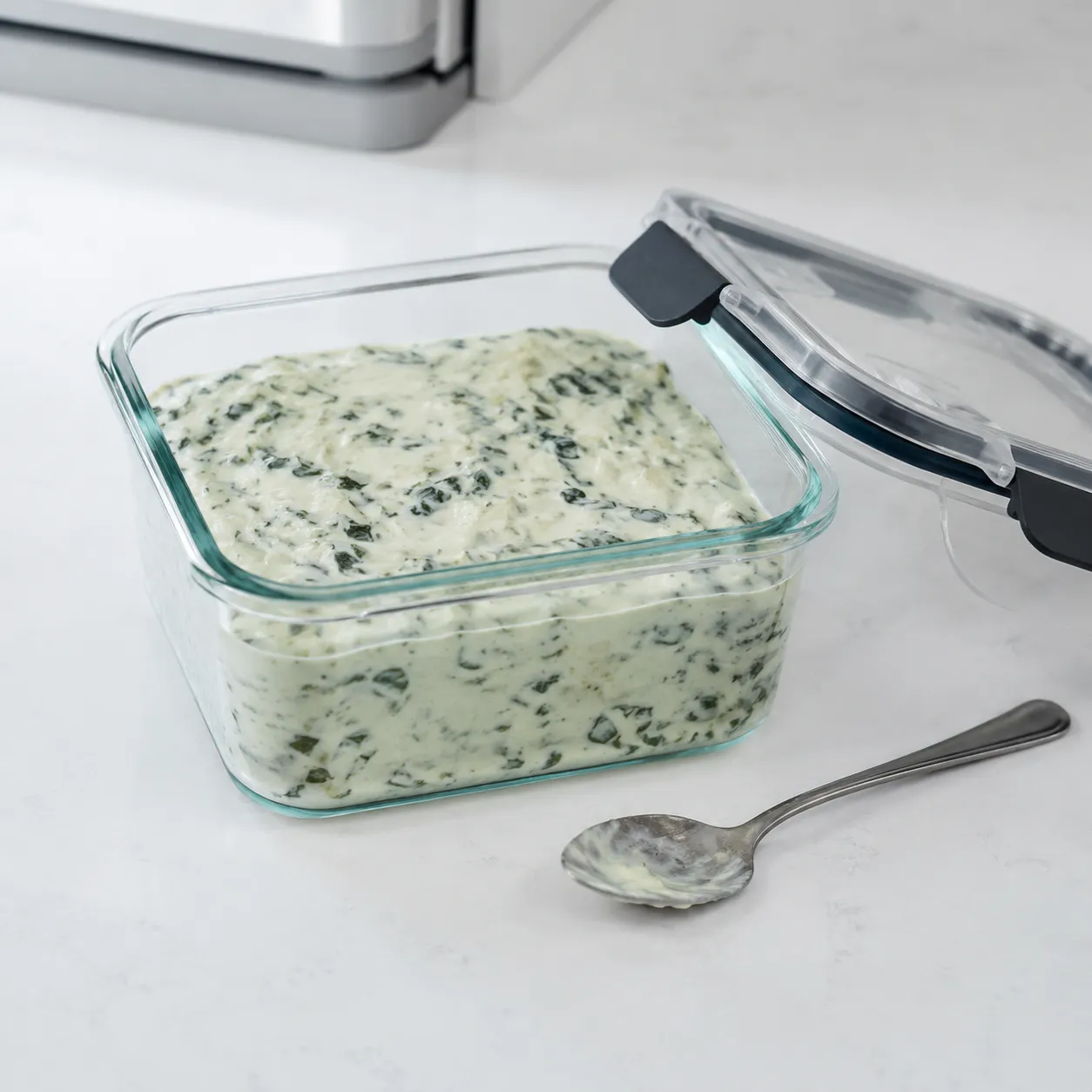 Spinach dip stored in a glass container for refrigerator storage