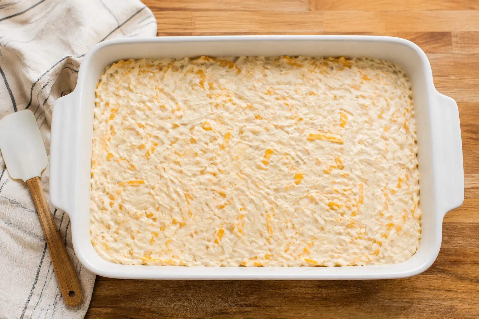 Unbaked hashbrown casserole spread in a white 9x13 baking dish