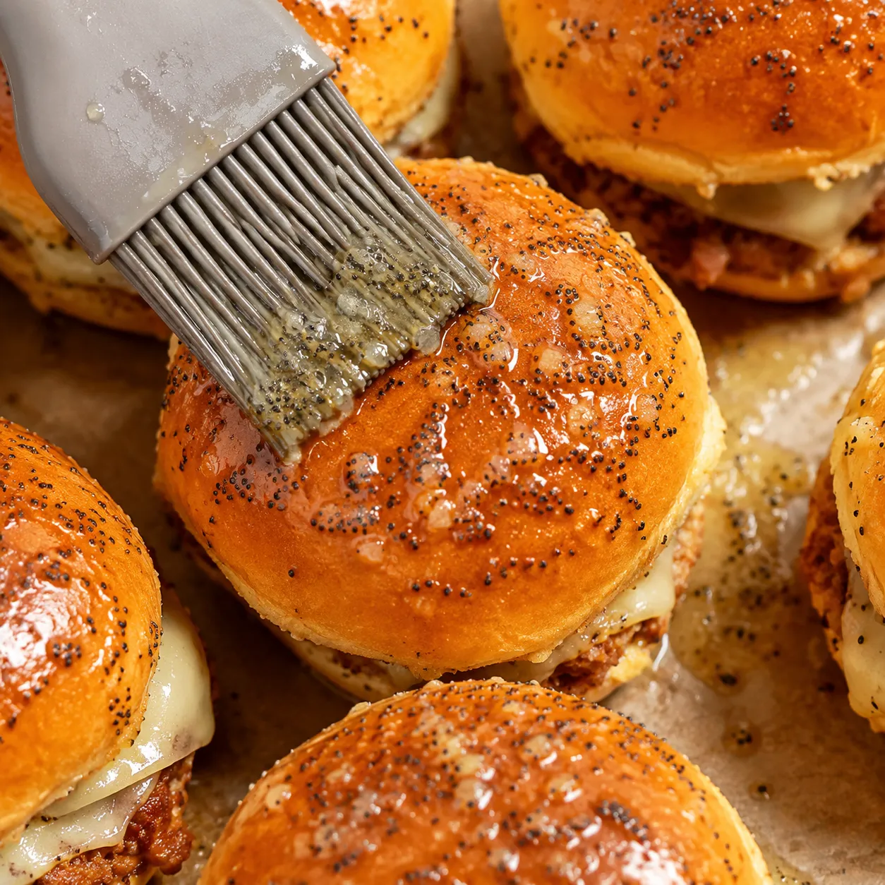 Brushing poppy seed butter glaze on ham and cheese sliders