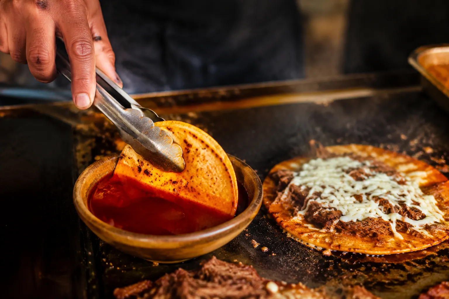 Dipping corn tortilla in birria fat to make crispy quesabirria tacos