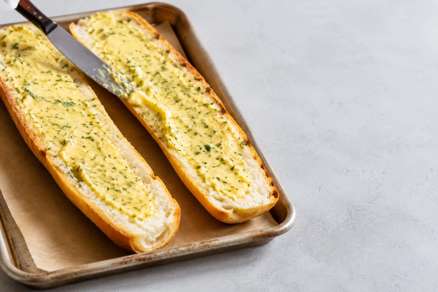 Spreading garlic butter on French bread for easy garlic bread recipe