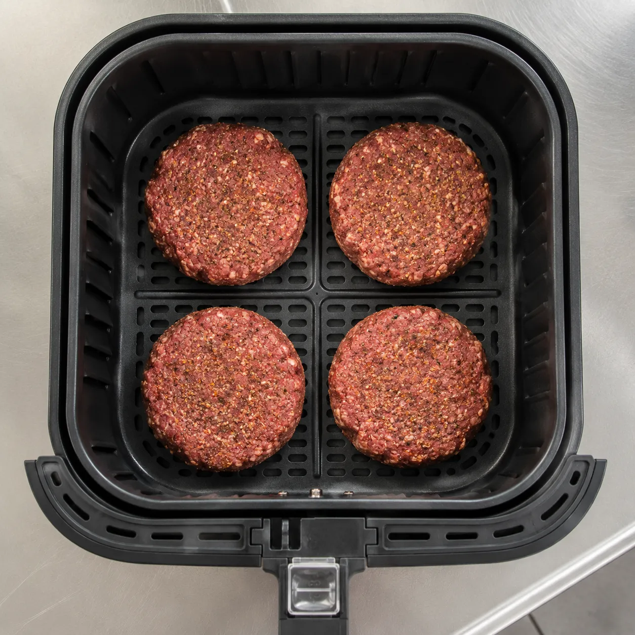 Raw seasoned patties arranged in air fryer basket for hamburgers in air fryer