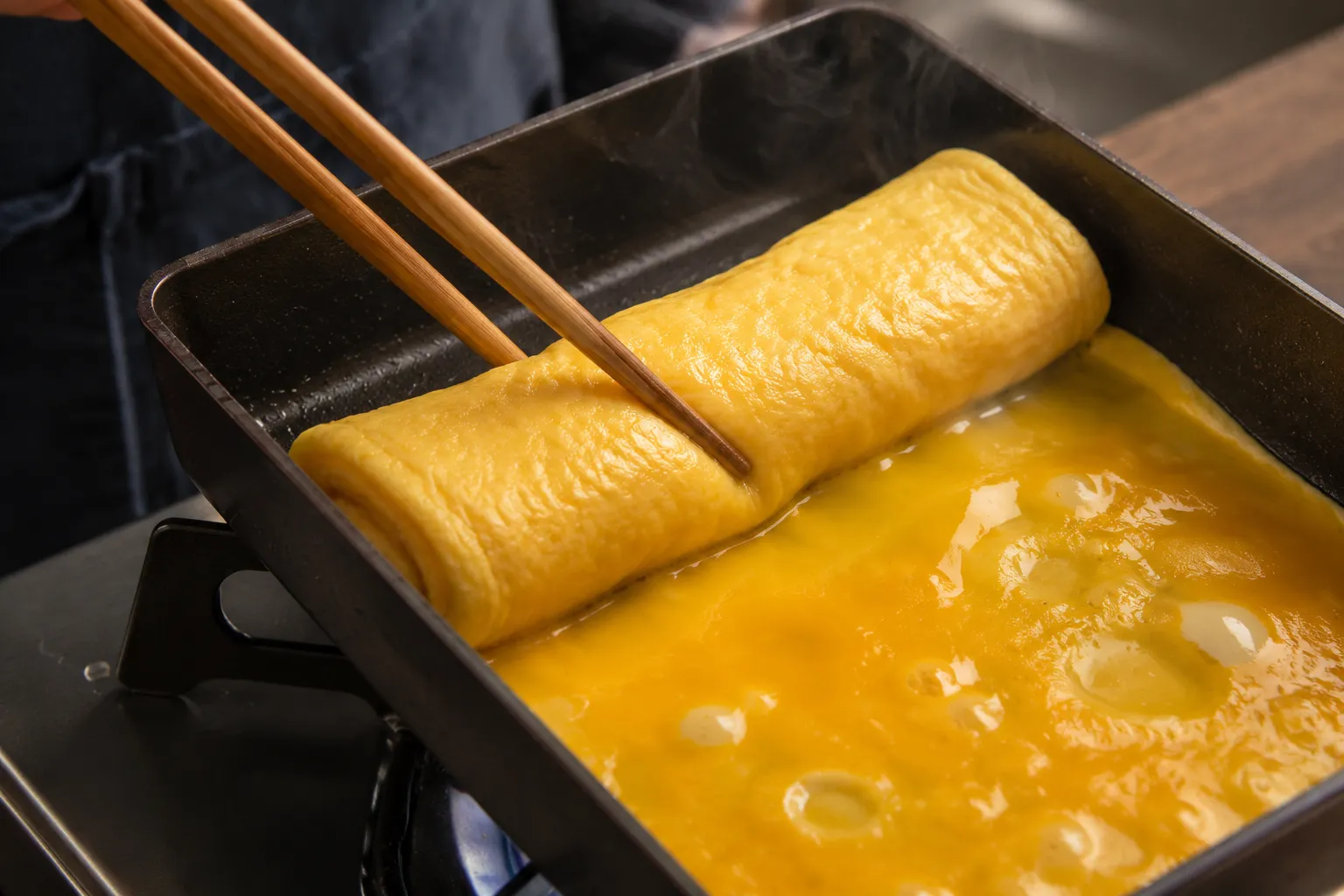 Rolling tamago layers with chopsticks in a Japanese omelet pan