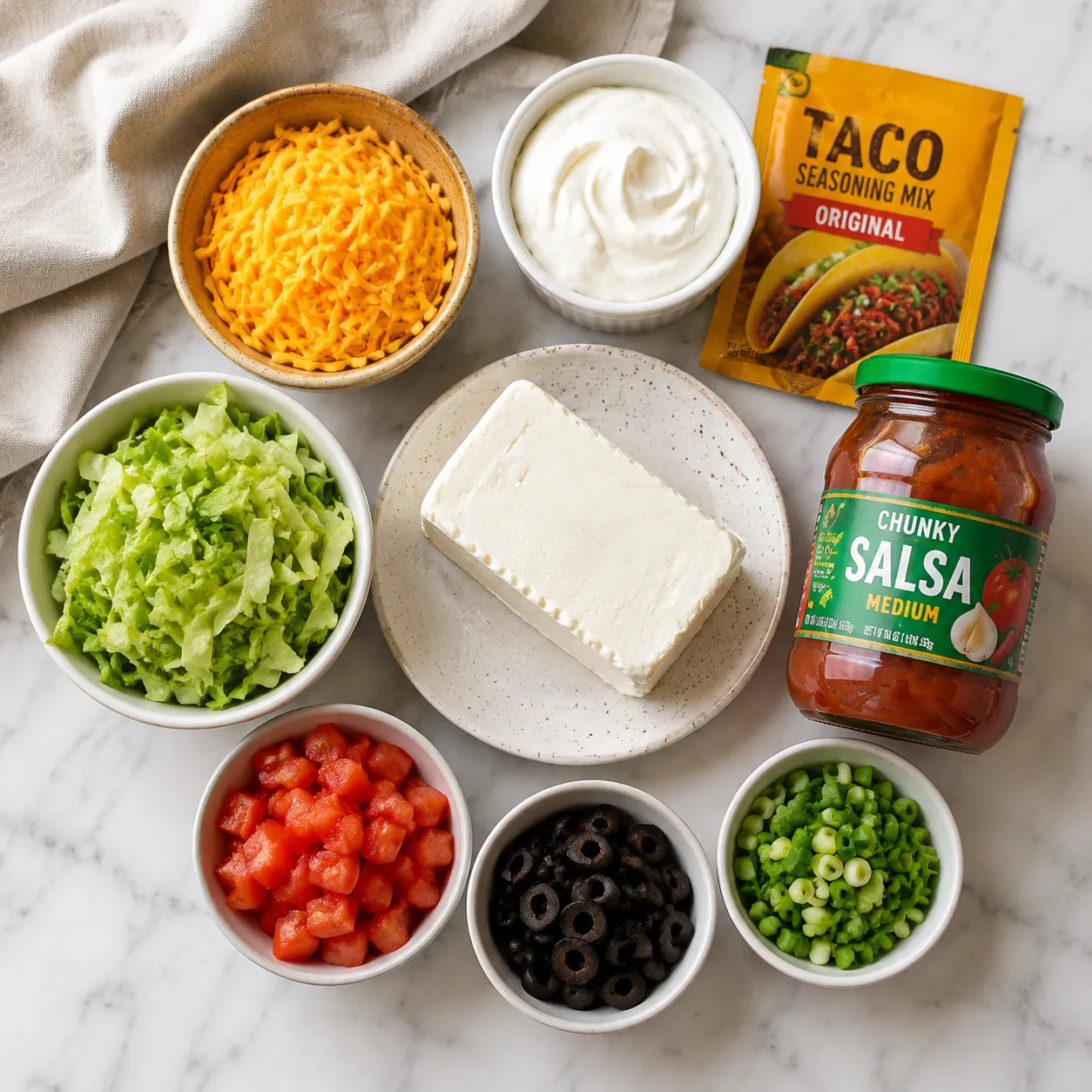 Layered taco dip ingredients flatlay with cream cheese, salsa, and cheddar
