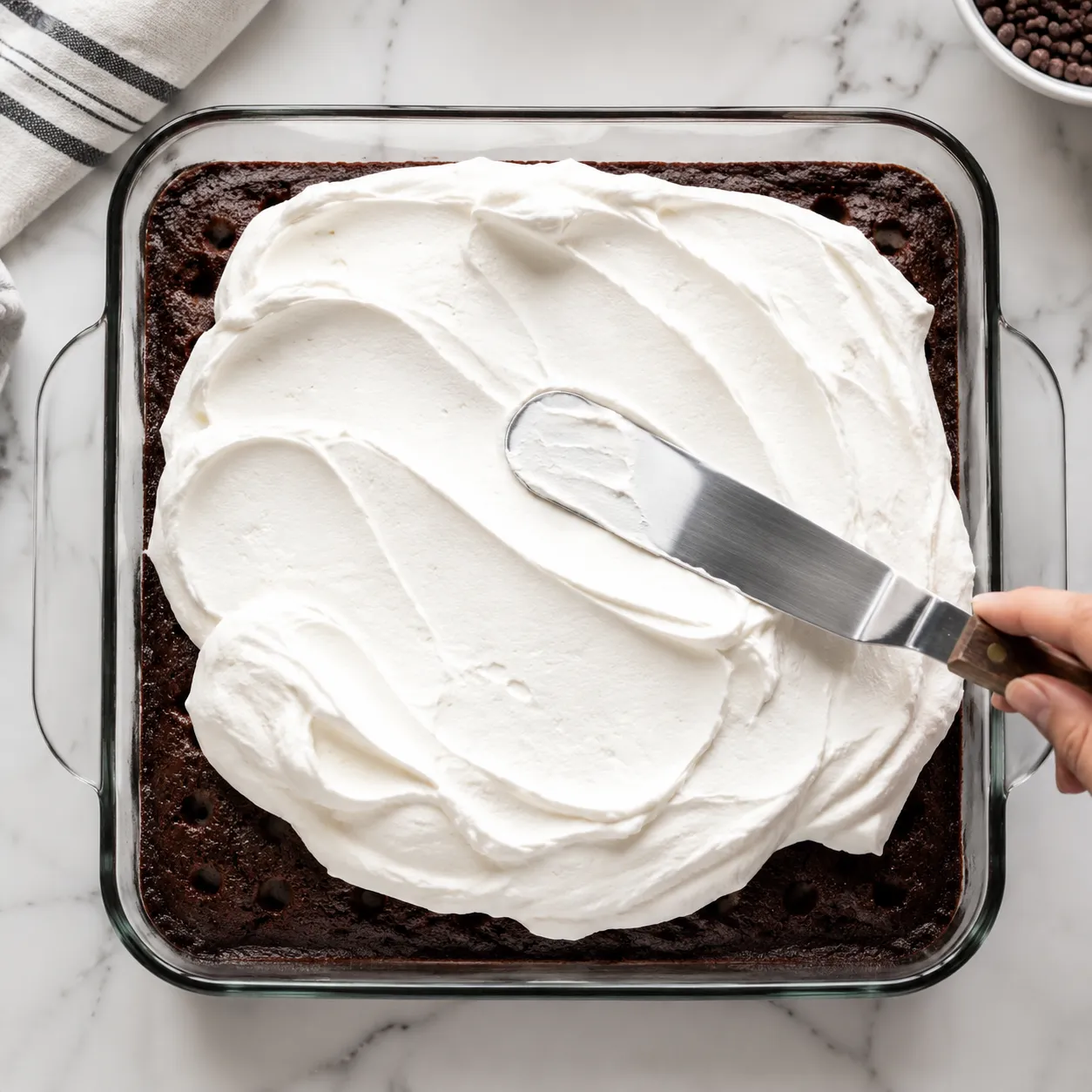 Spreading whipped topping over caramel poke cake