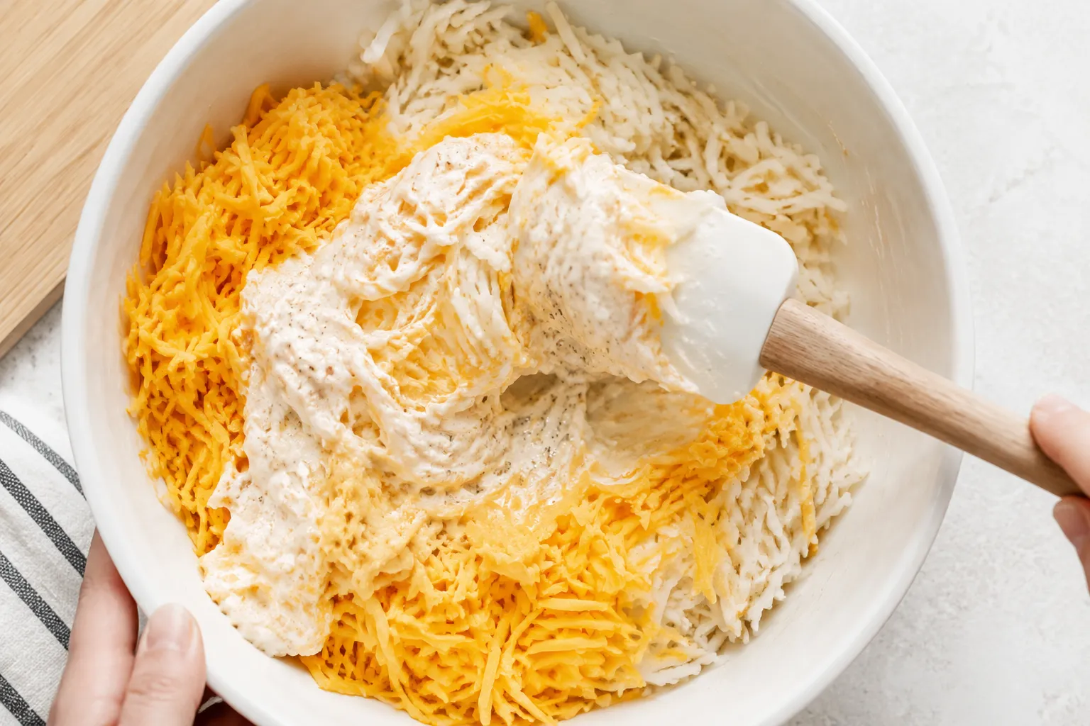 Folding cheddar cheese into hash browns for cheesy hashbrown potatoes