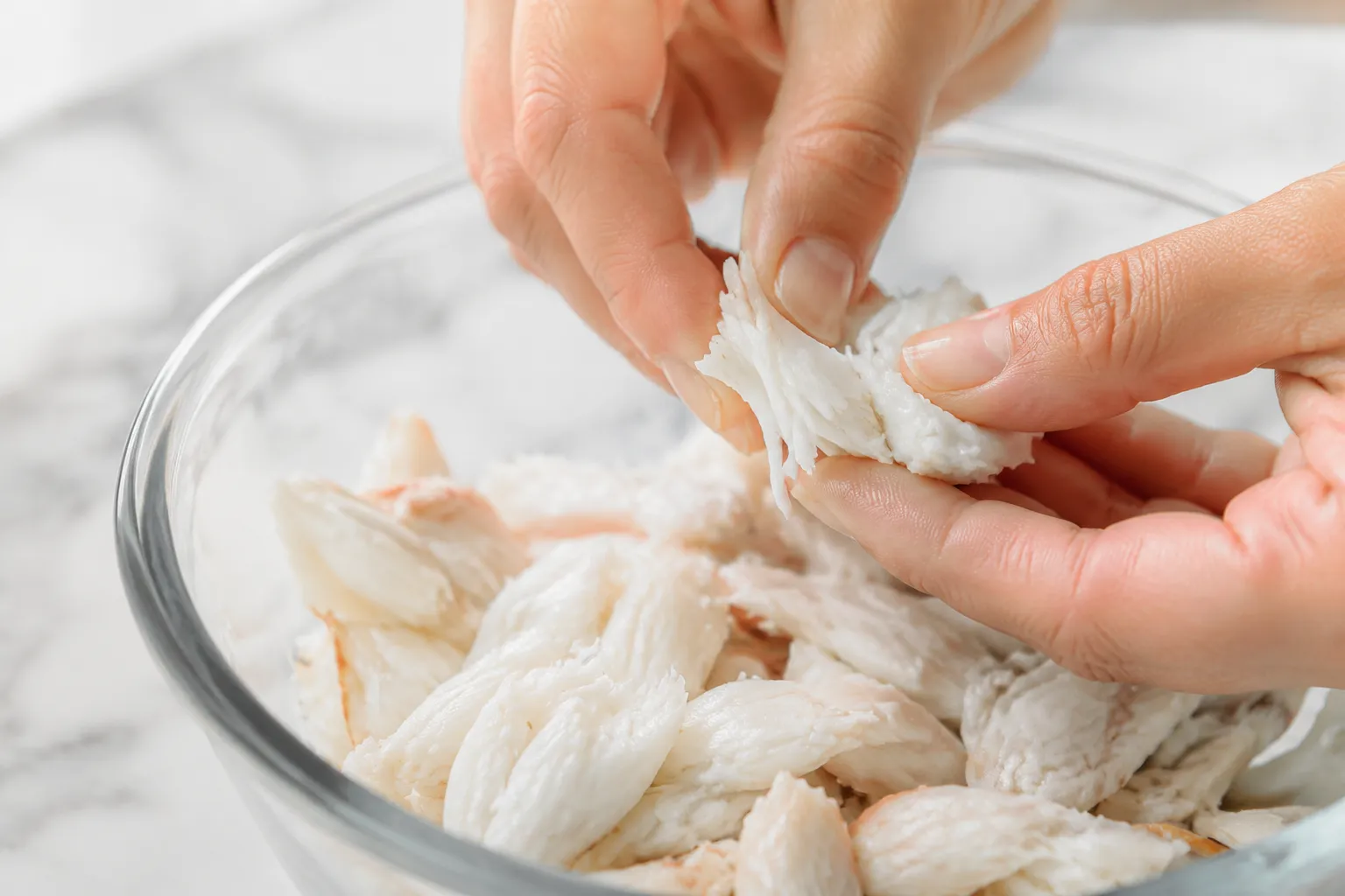Hands flaking lump crab meat in a glass bowl for crab salad recipe