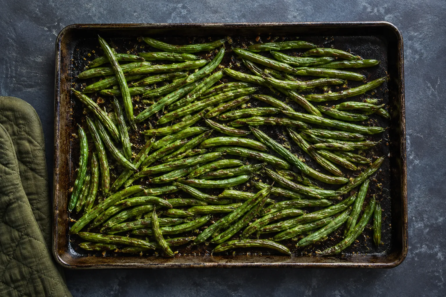 Green beans spread on a sheet pan ready to bake at 425F
