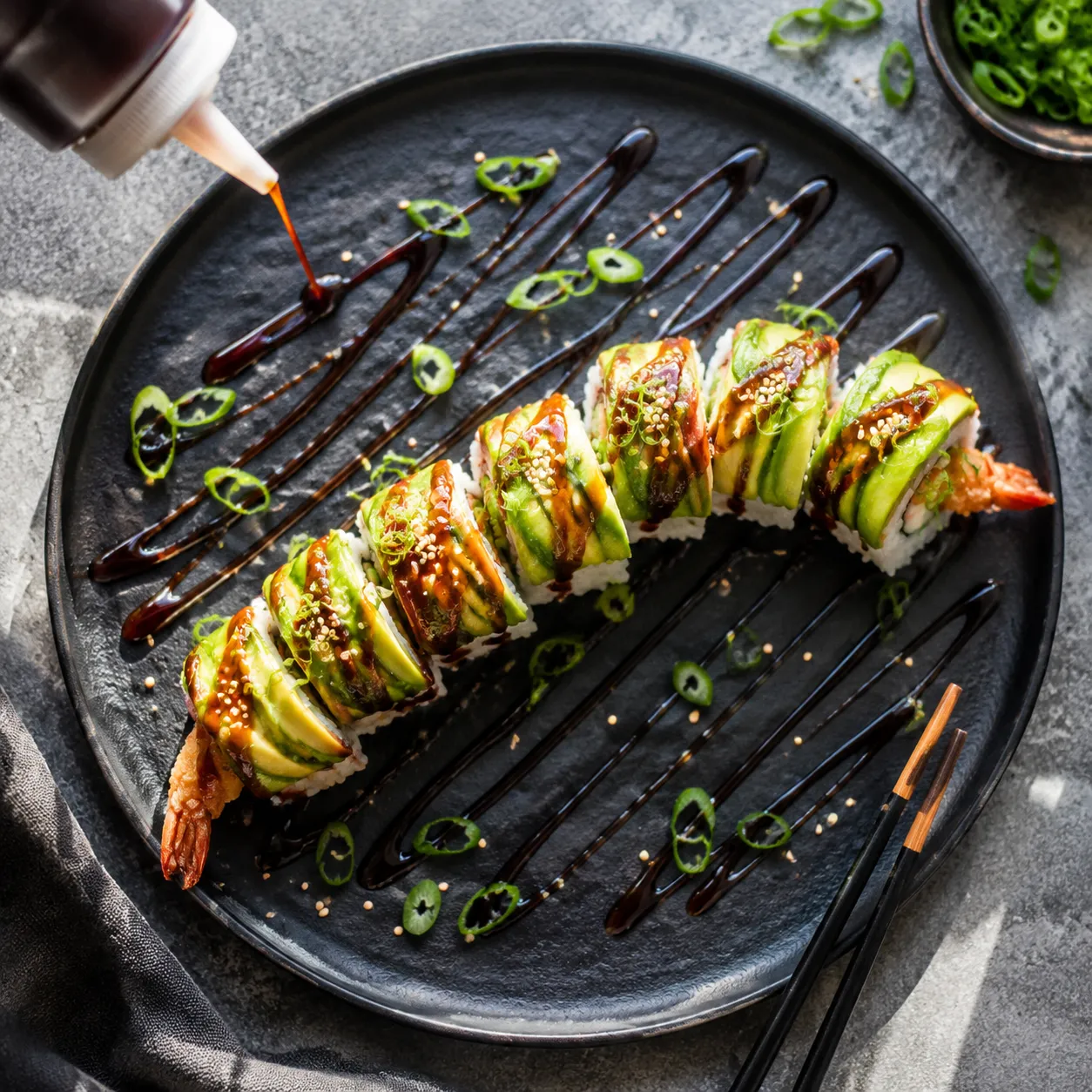 Drizzling eel sauce over fresh sushi rolls topped with sesame and scallion