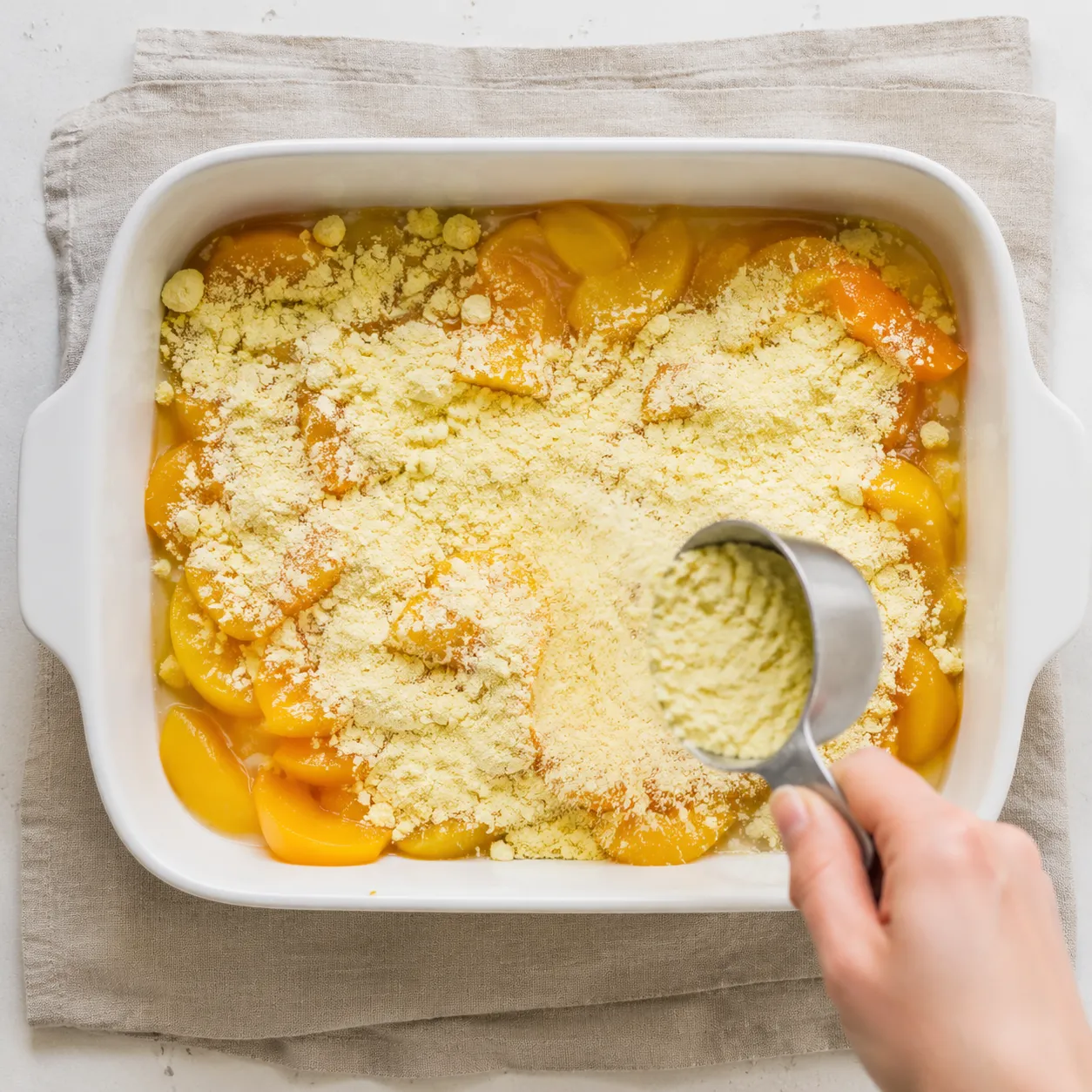 Sprinkling yellow cake mix over peaches for a peach cobbler dump cake.