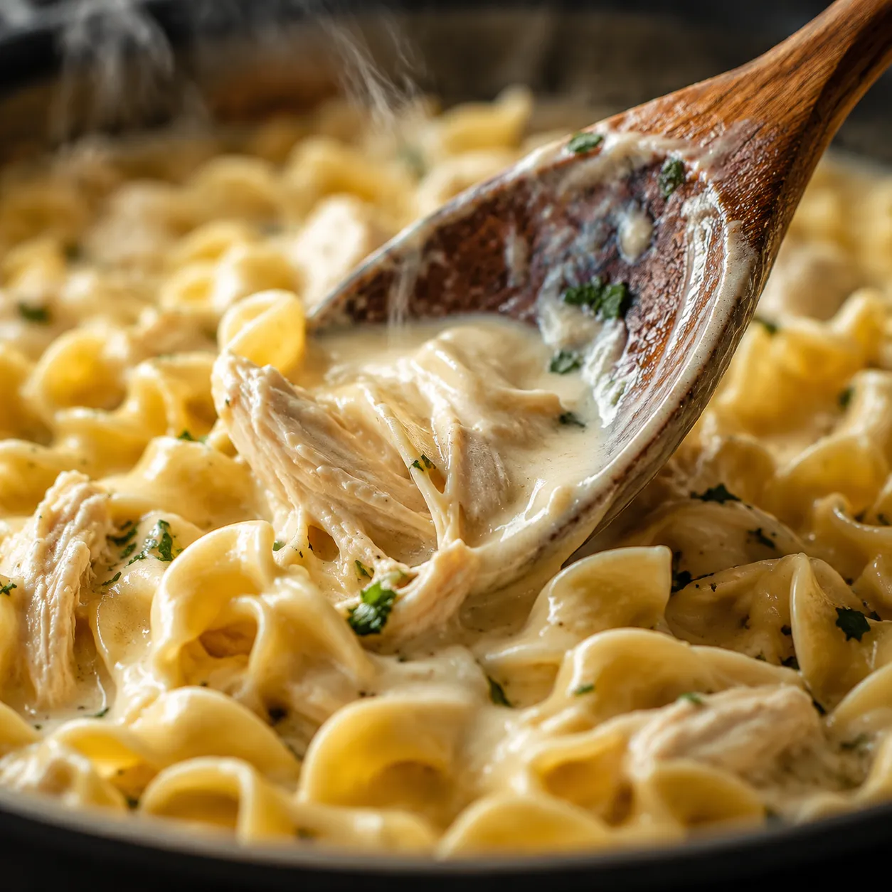 Stirring shredded chicken and cream into homestyle chicken and noodles