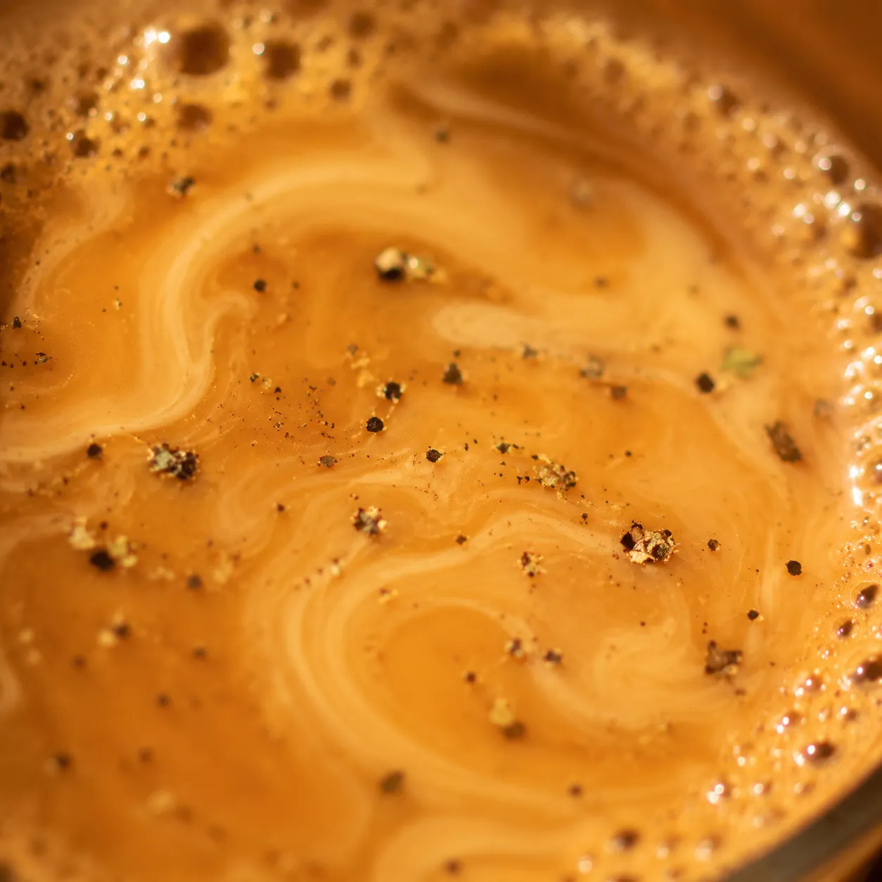 Close-up of creamy masala chai surface with spice flecks