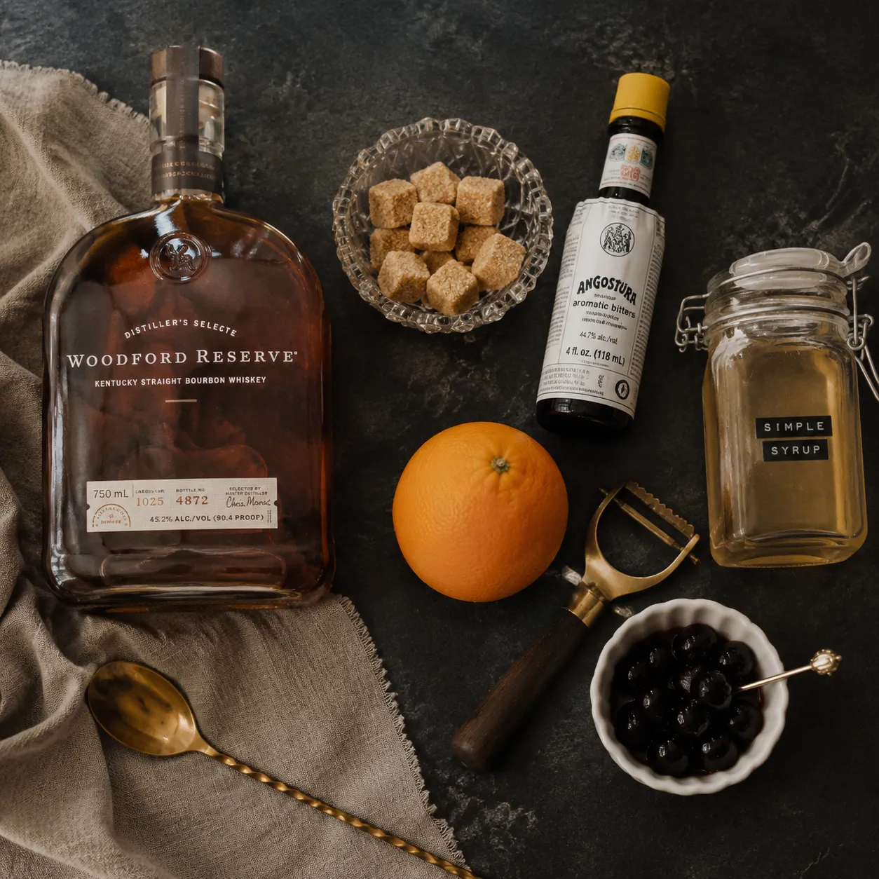 Bourbon old fashioned ingredients flatlay with bourbon, bitters, sugar, and orange