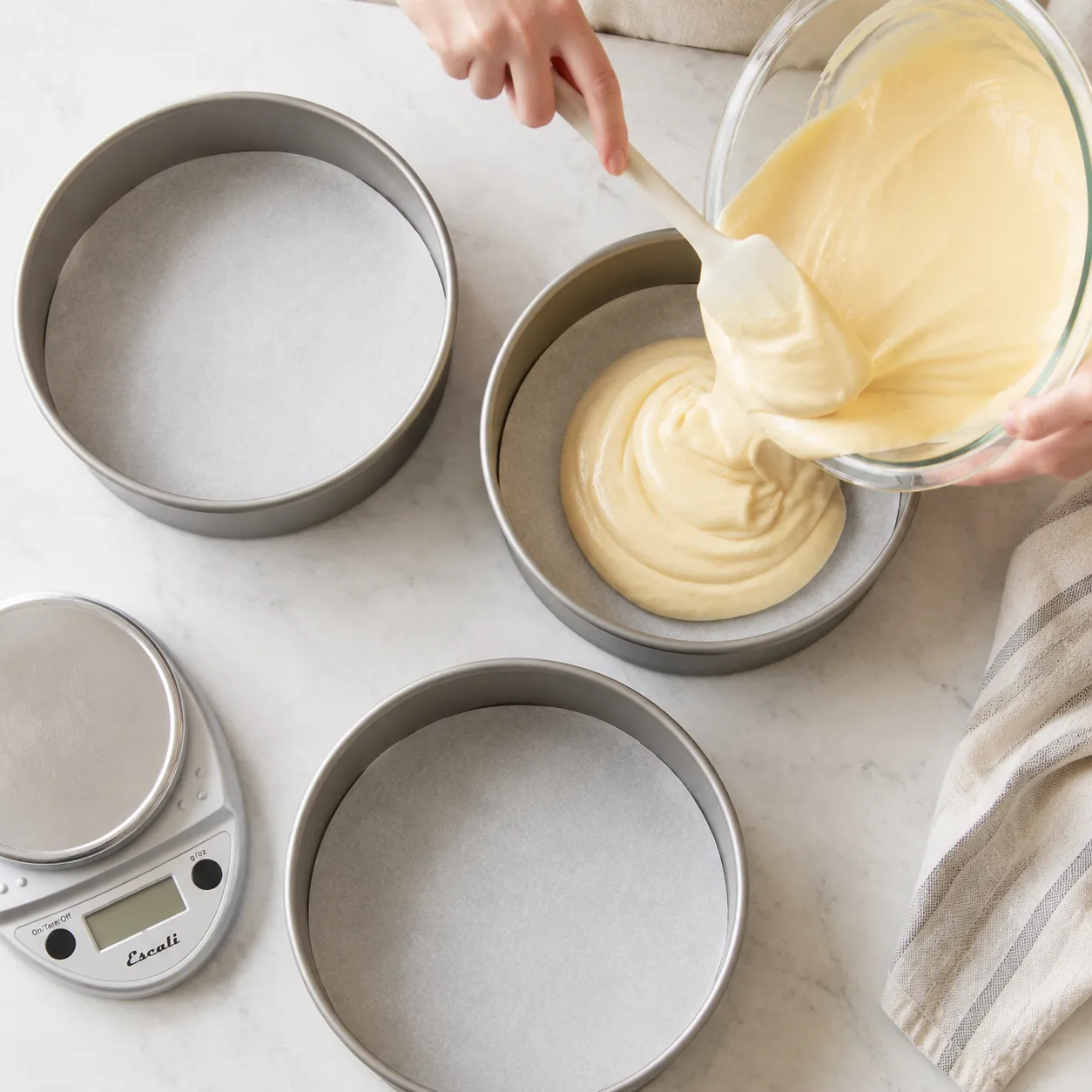 Dividing white cake batter into three round pans