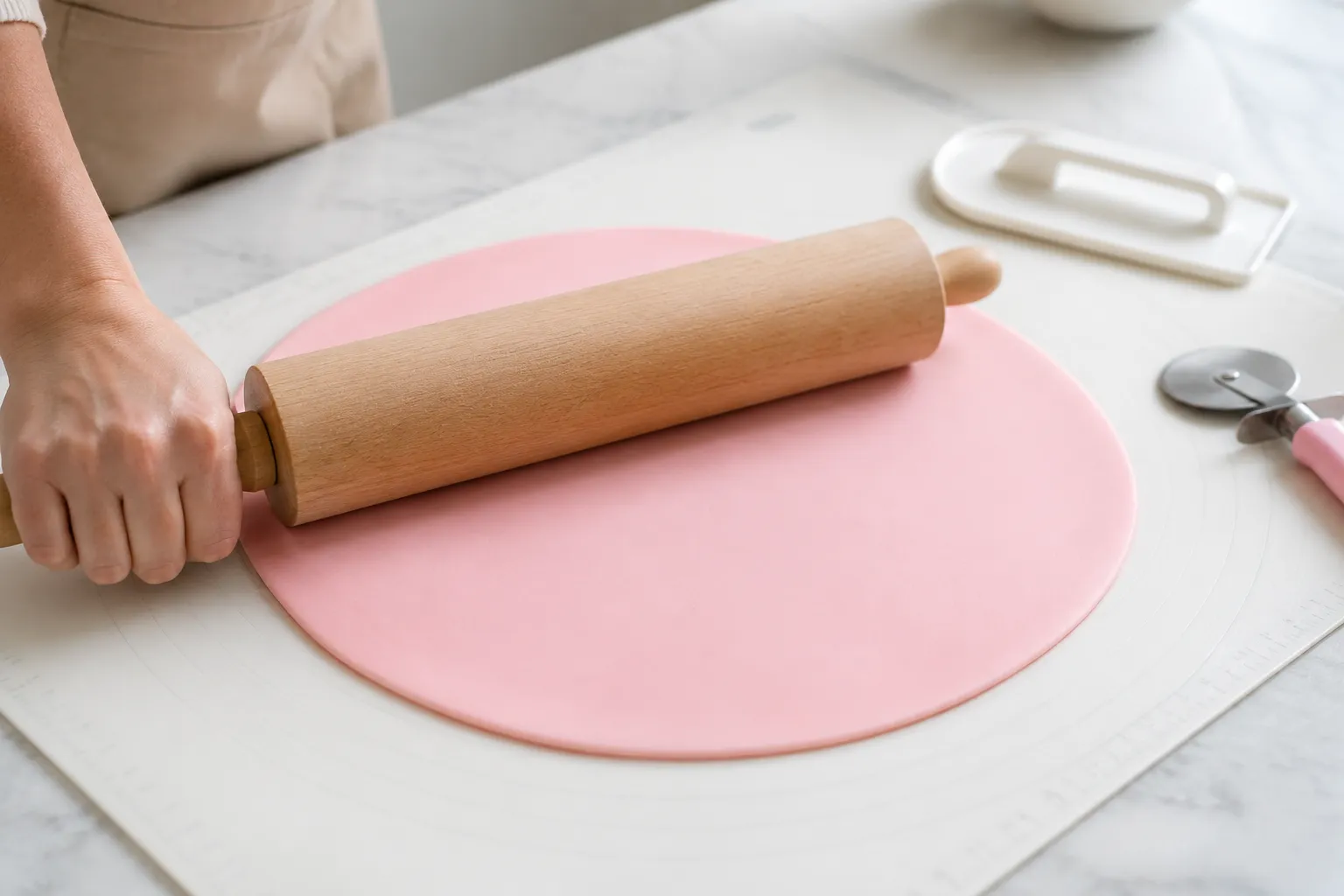 Rolling out pink fondant with a wooden rolling pin for cake decorating