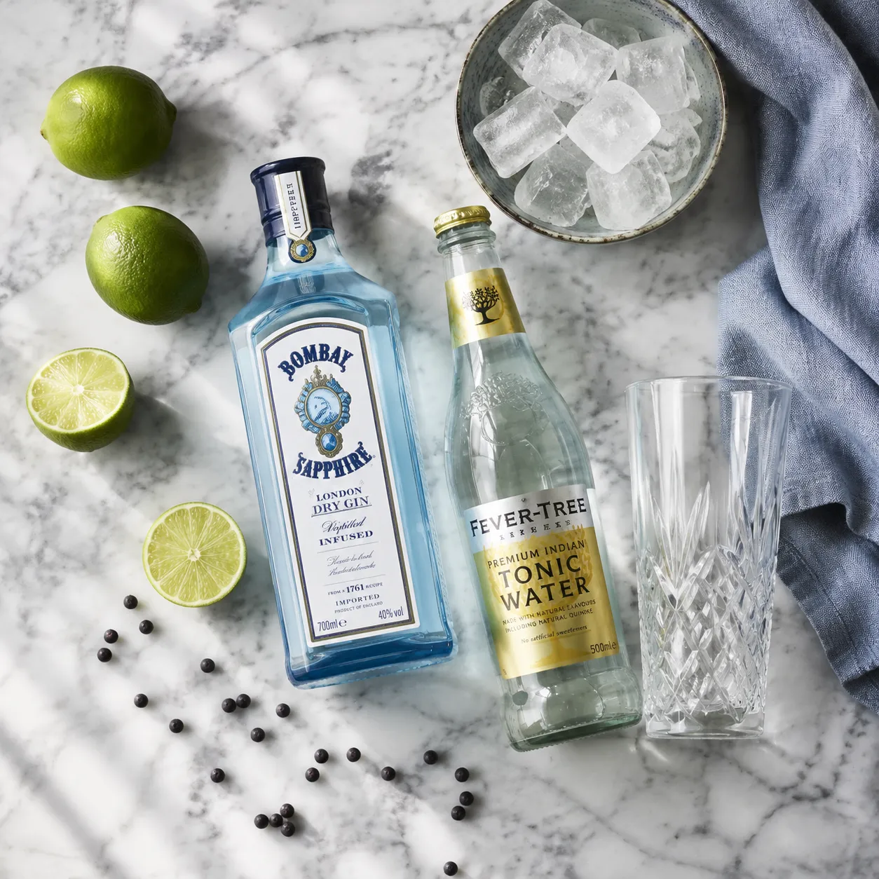Gin and tonic recipe ingredients flatlay with gin, tonic water, lime, and juniper.