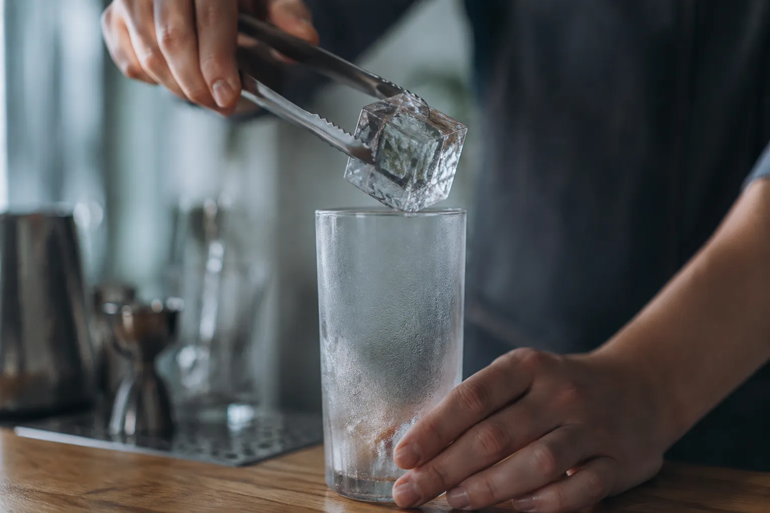Adding large clear ice cubes to a highball glass for gin and tonic.