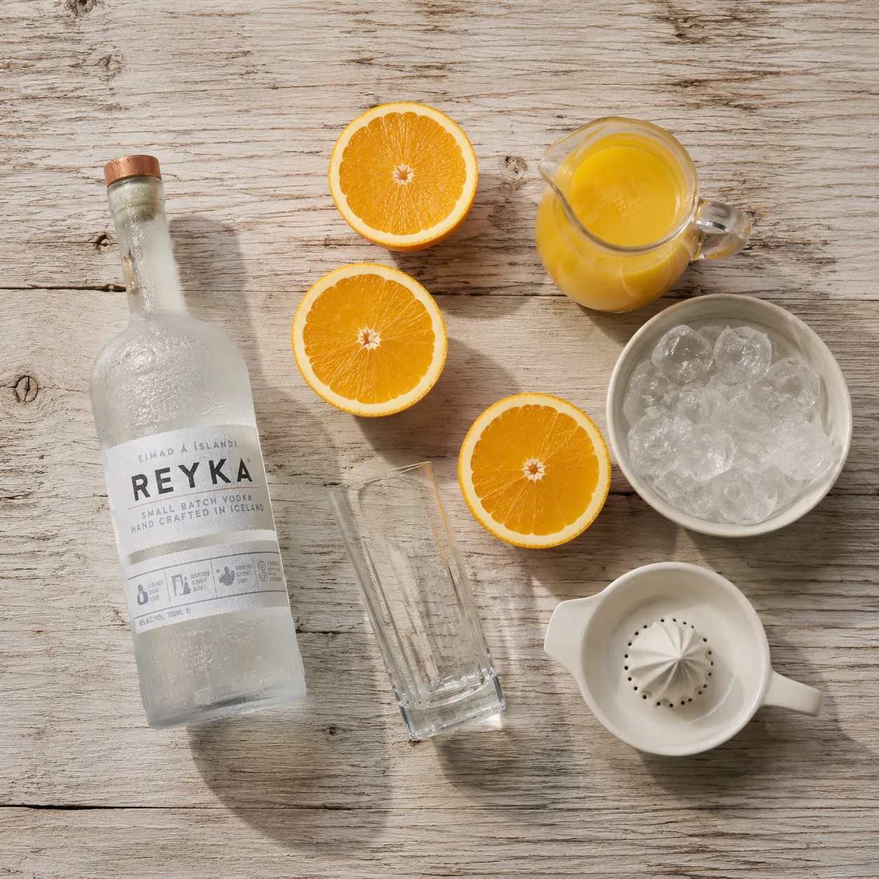 Screwdriver drink ingredients flatlay with vodka, fresh oranges, and ice