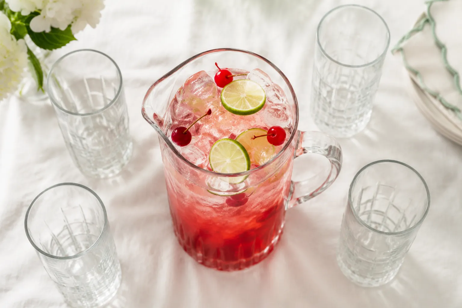 Pitcher of dirty Shirley cocktail for a party with cherries and lime