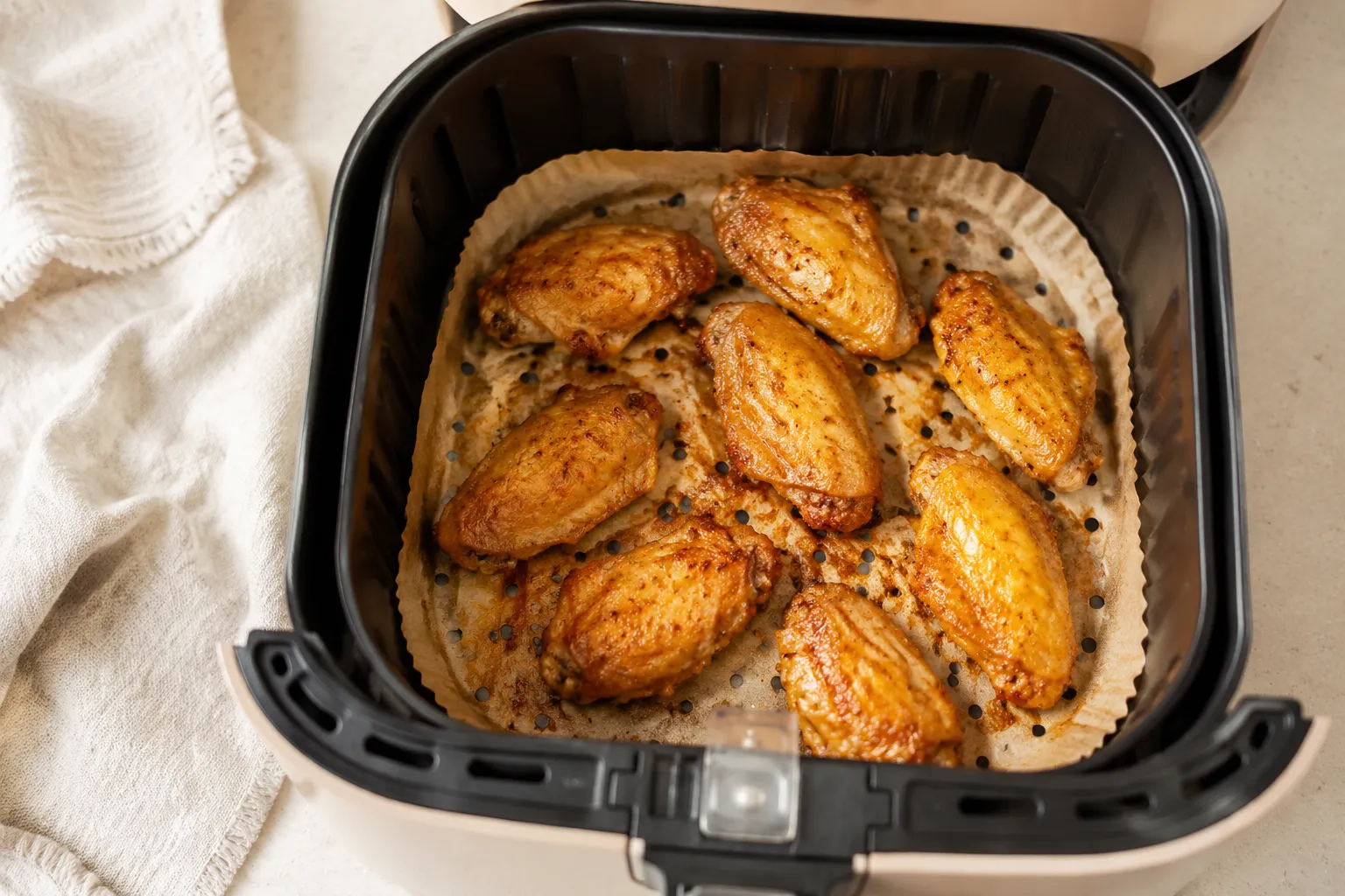 Finished crispy wings on parchment paper in air fryer with no mess