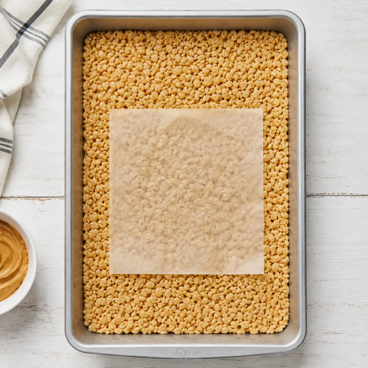 Peanut butter cereal pressed into pan for scotcharoos