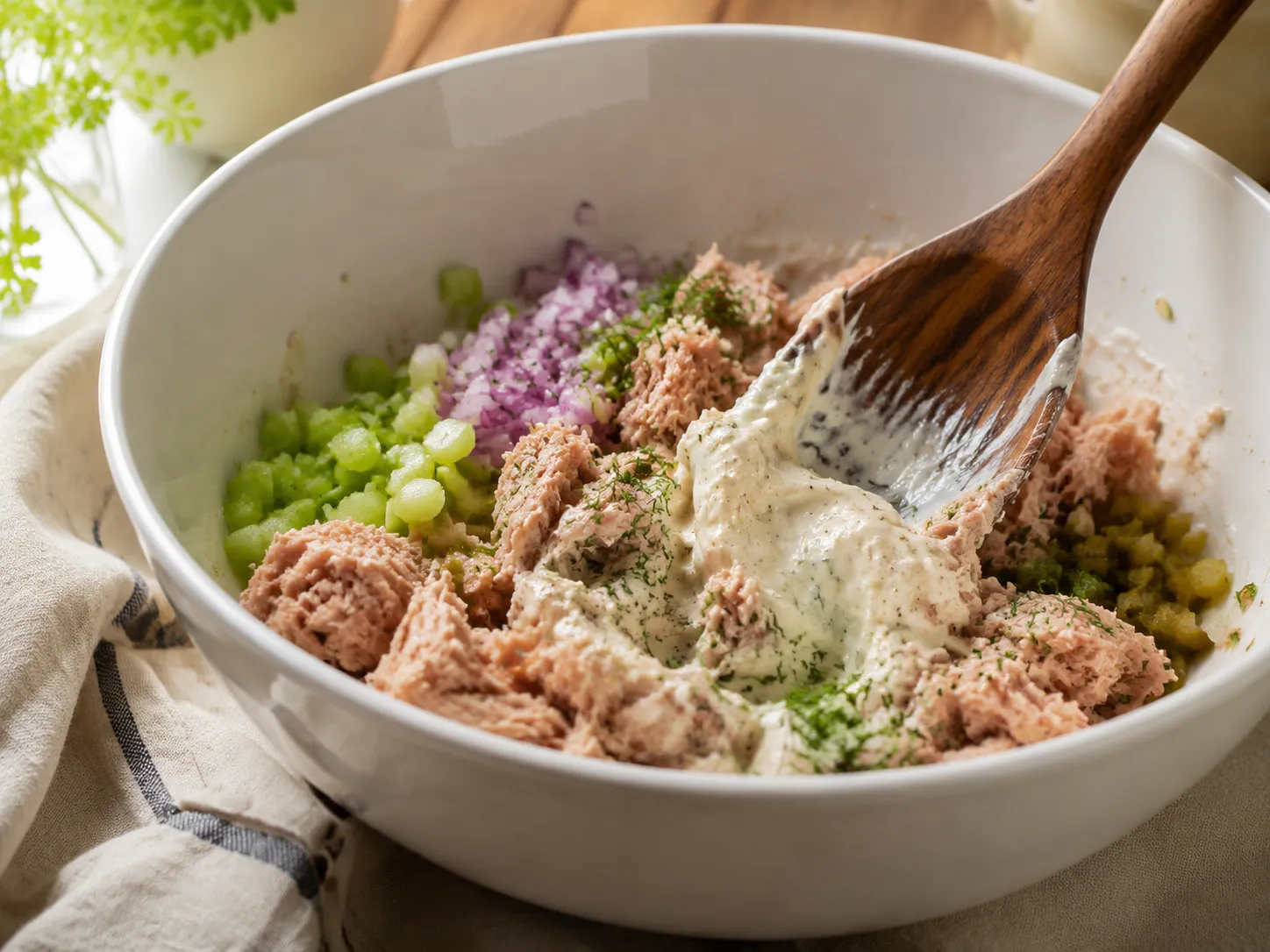 Folding tuna salad ingredients together in a mixing bowl