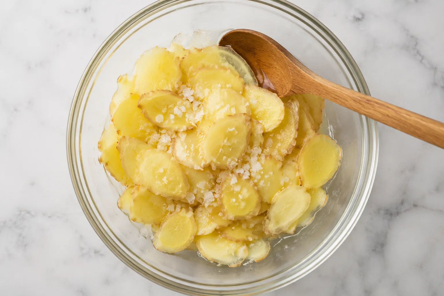 Salted ginger slices resting in a glass bowl before pickling
