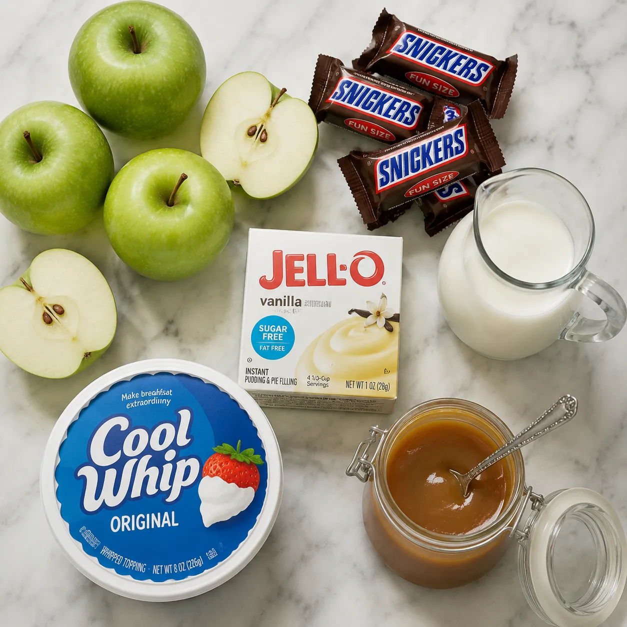 Snickers salad ingredients flatlay including apples, candy bars, pudding mix, and Cool Whip
