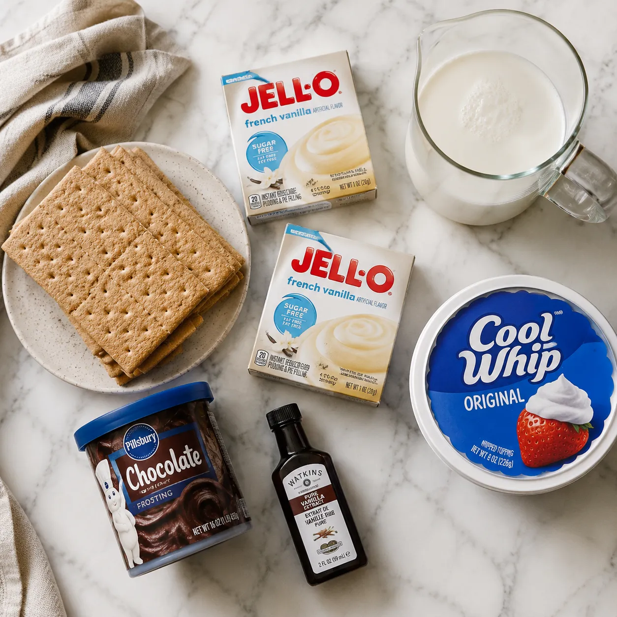 Eclair cake ingredients flatlay with graham crackers, pudding mix, milk, and chocolate frosting