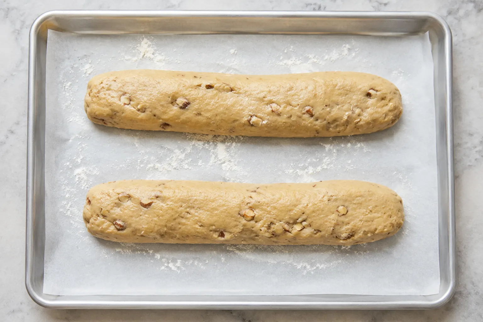 Shaped biscotti logs on a parchment-lined baking sheet before the first bake