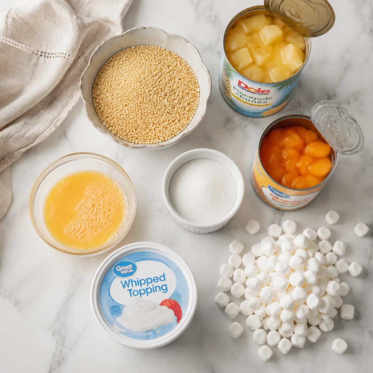 Frog eye salad ingredients flatlay with acini di pepe pasta, pineapple, mandarin oranges, and marshmallows