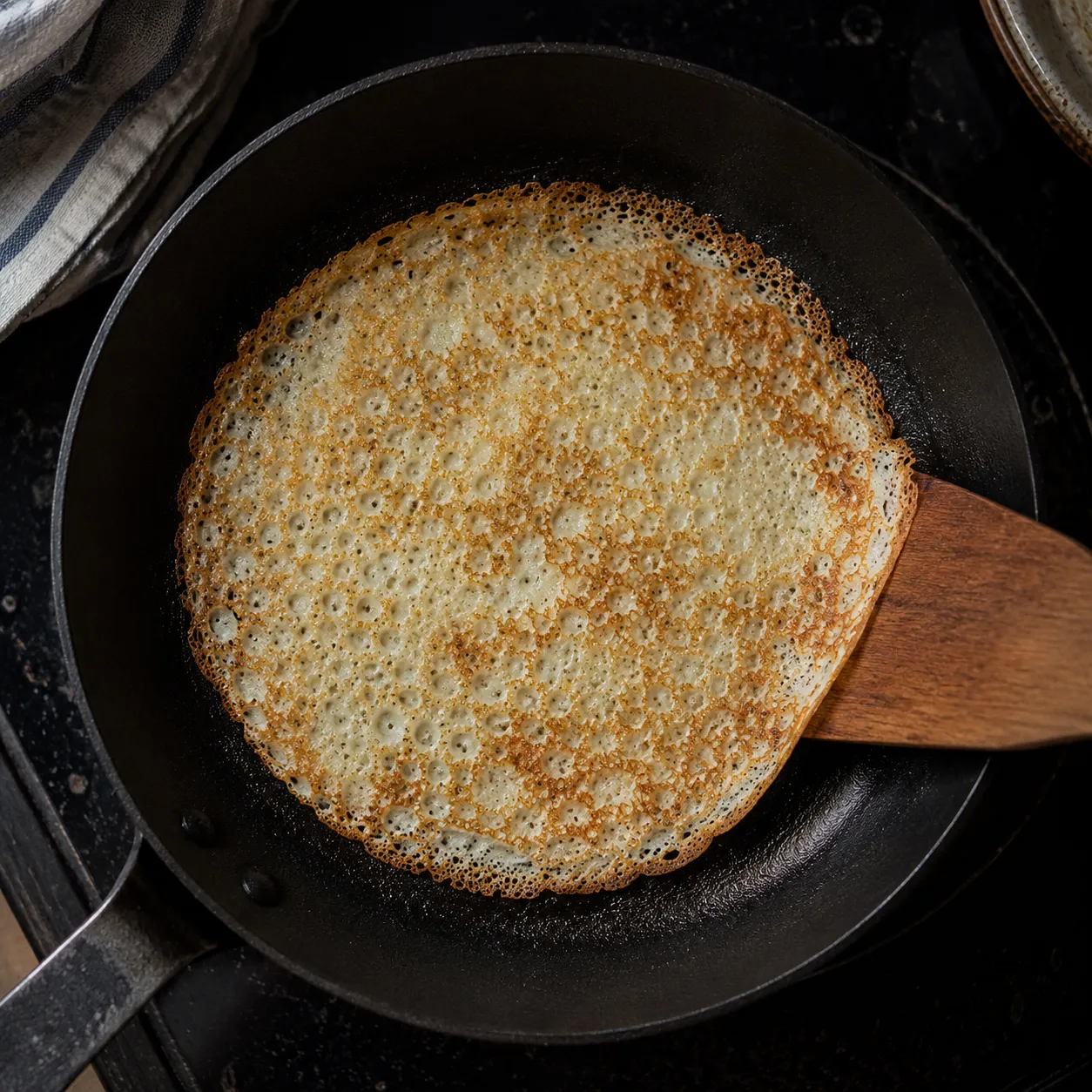 Thin Swedish pancake cooking in a skillet with golden lacy edges